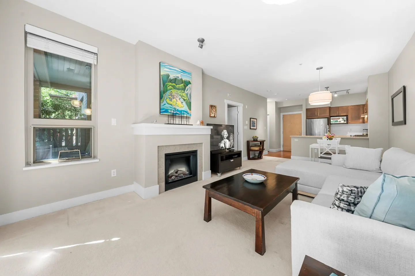 Open-concept living room with a fireplace, white sofa, dark coffee table, and a view into the kitchen.