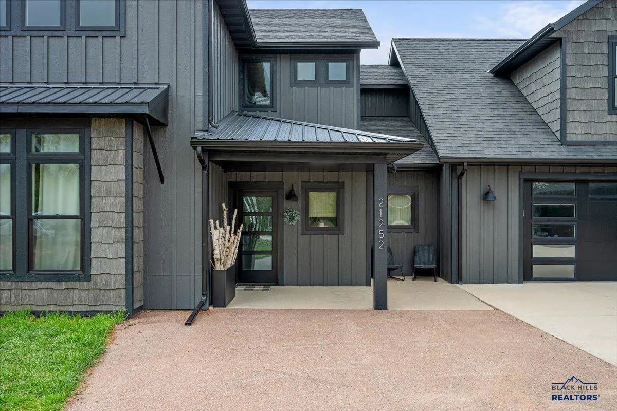 Modern dark gray home exterior with a covered porch, glass front door, and a concrete driveway under a clear blue sky.