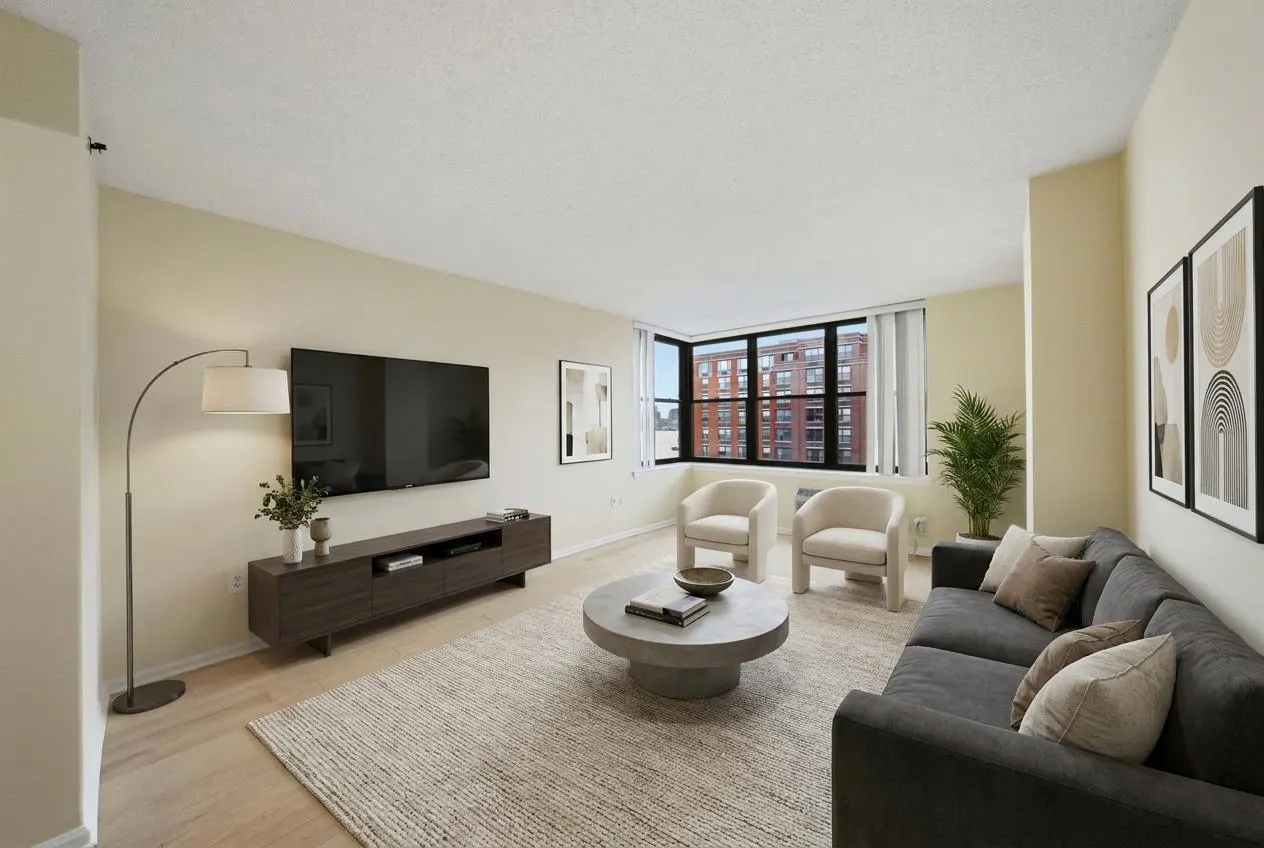 Modern living room with a dark grey sofa, two cream armchairs, a round coffee table, and a wall-mounted TV on a wood console.