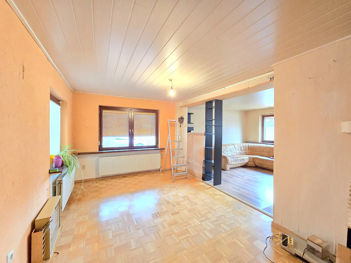 A bright, empty room with orange walls, a wooden floor, and a ladder. A black bookshelf divides the room.