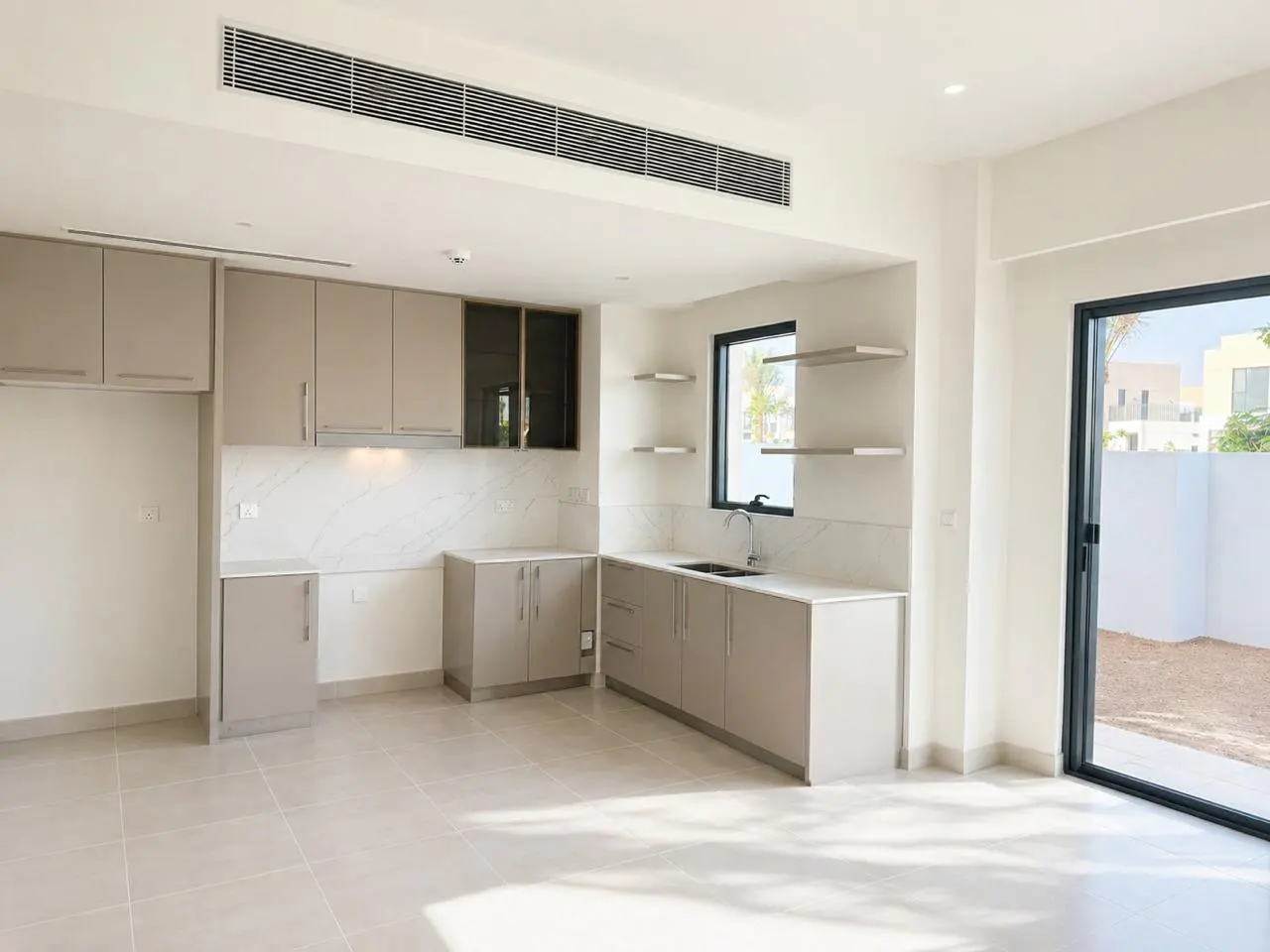 Bright, empty kitchen with beige cabinets, marble countertops, and tile floor. A sliding glass door leads to a fenced yard.