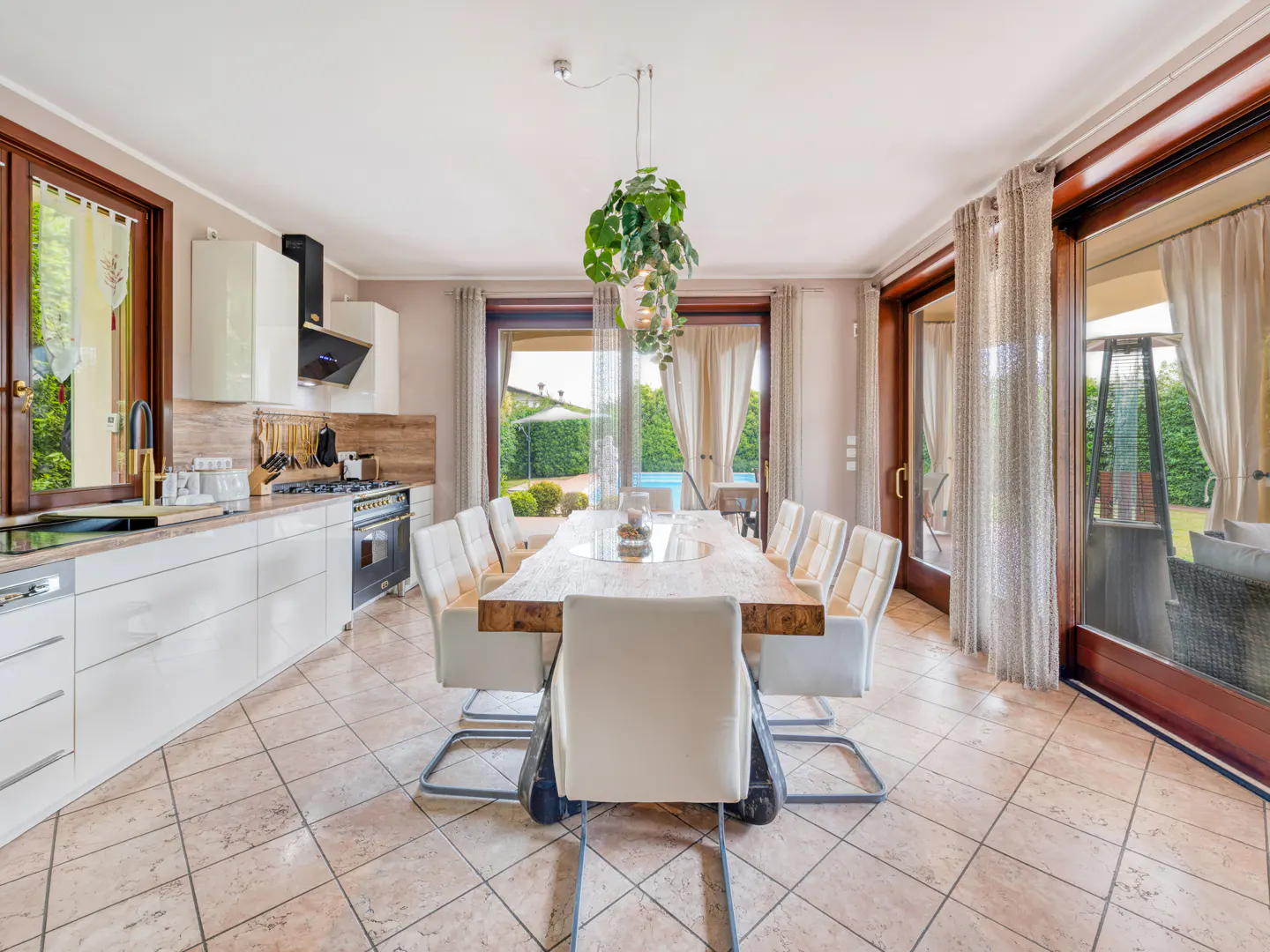 Modern kitchen and dining area with white cabinets, a rustic wooden table, white chairs, and large glass patio doors.