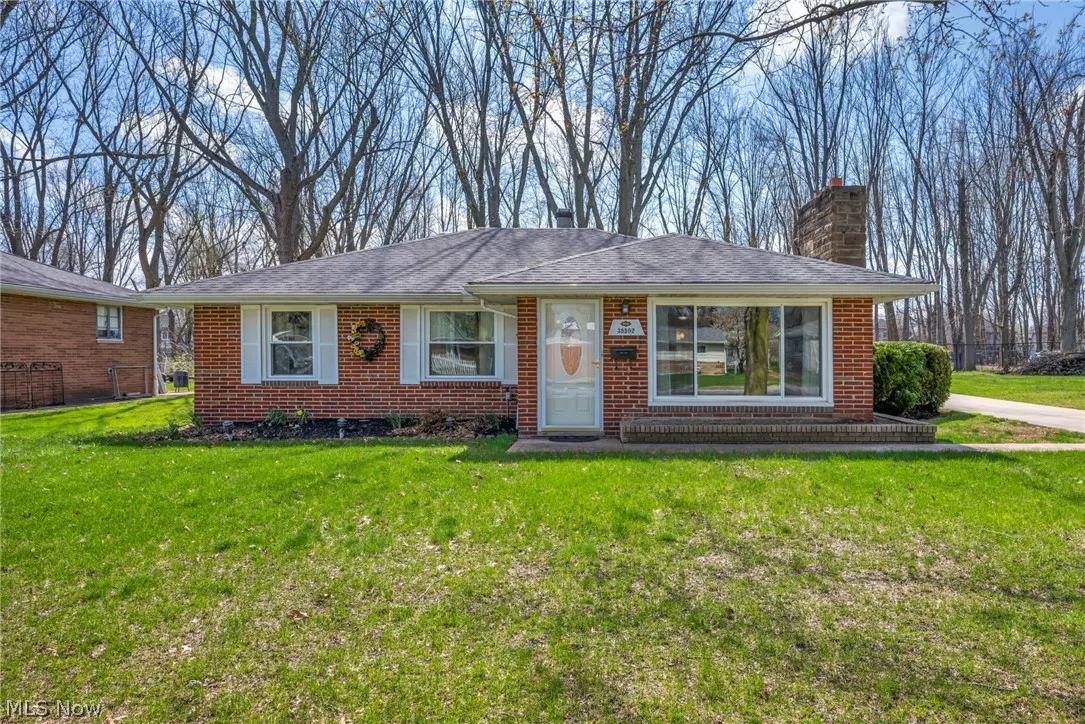 A single-story red brick house with white trim and a gray roof sits on a green lawn. Bare trees are in the background.