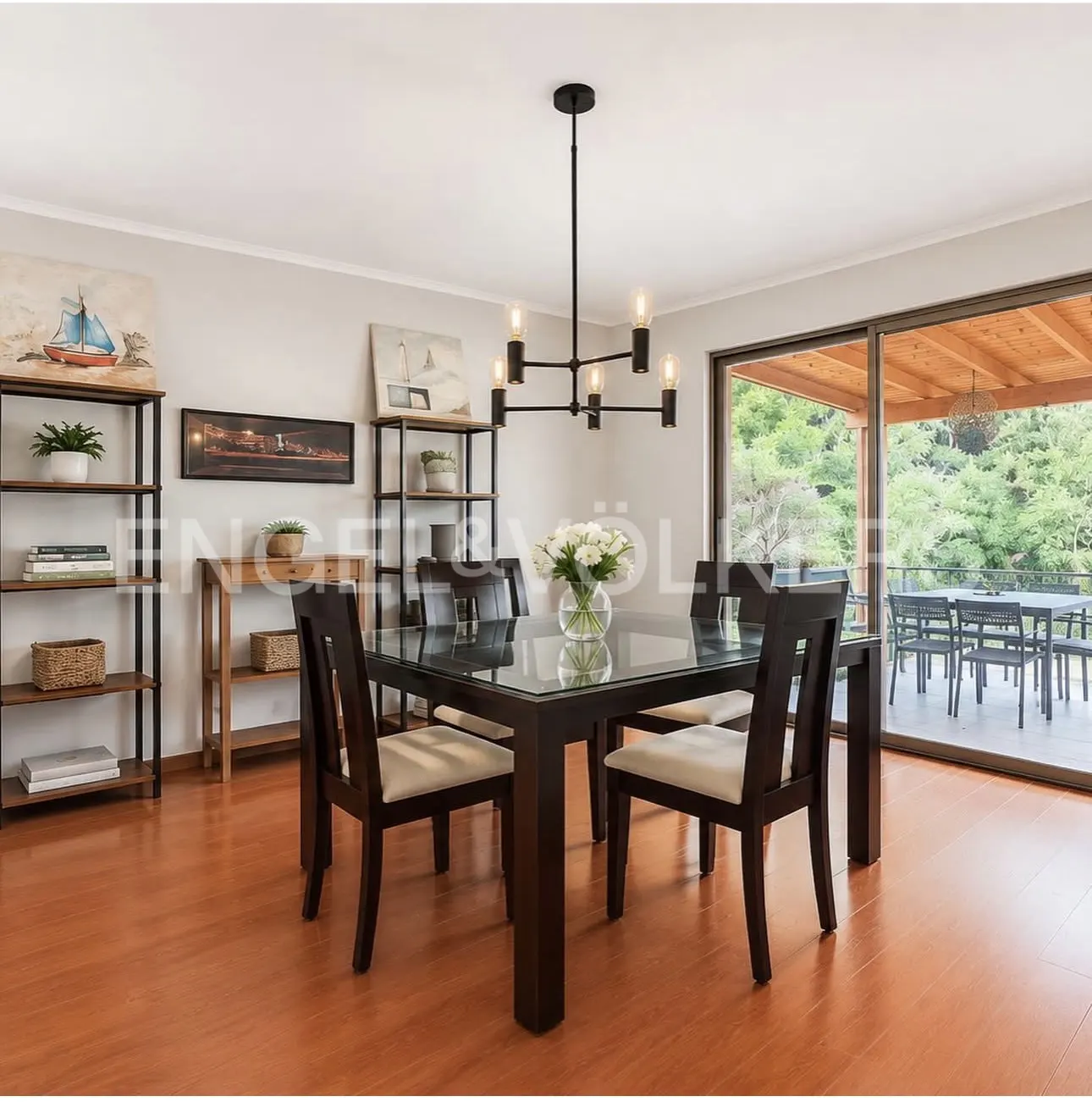 Dining room with wood floors, a glass-topped table with six chairs, and a black chandelier. Shelves with art and plants line the wall. Sliding glass doors open to a patio.