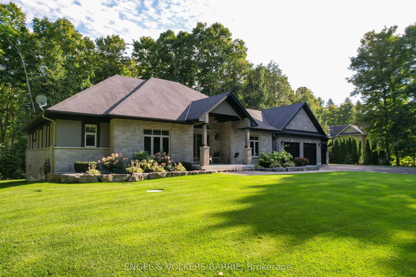 Stone house with dark roof and trim, surrounded by green lawn and trees under a blue sky.