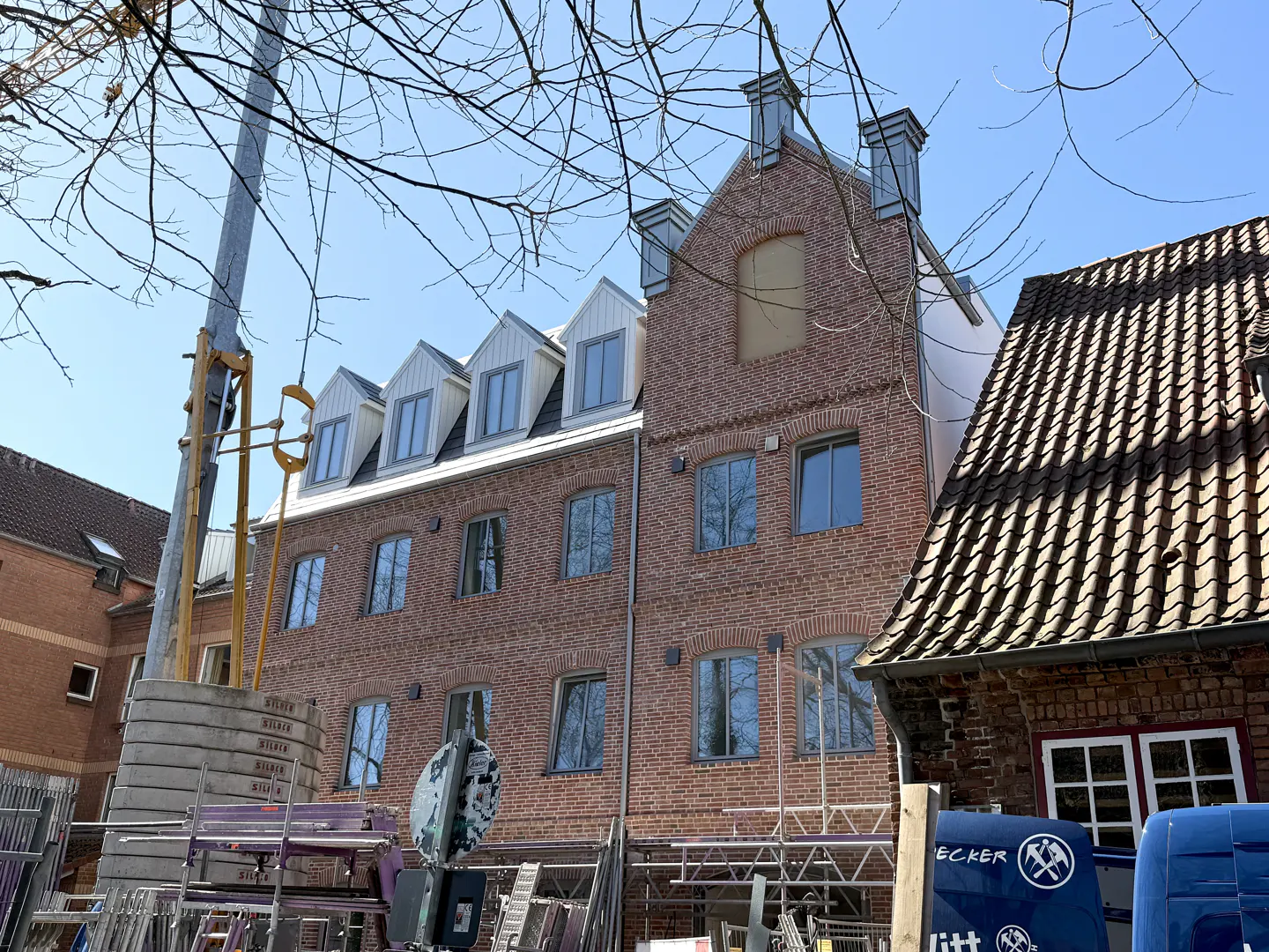 Exterior view of a red brick building with dormer windows under a blue sky, construction equipment in the foreground.