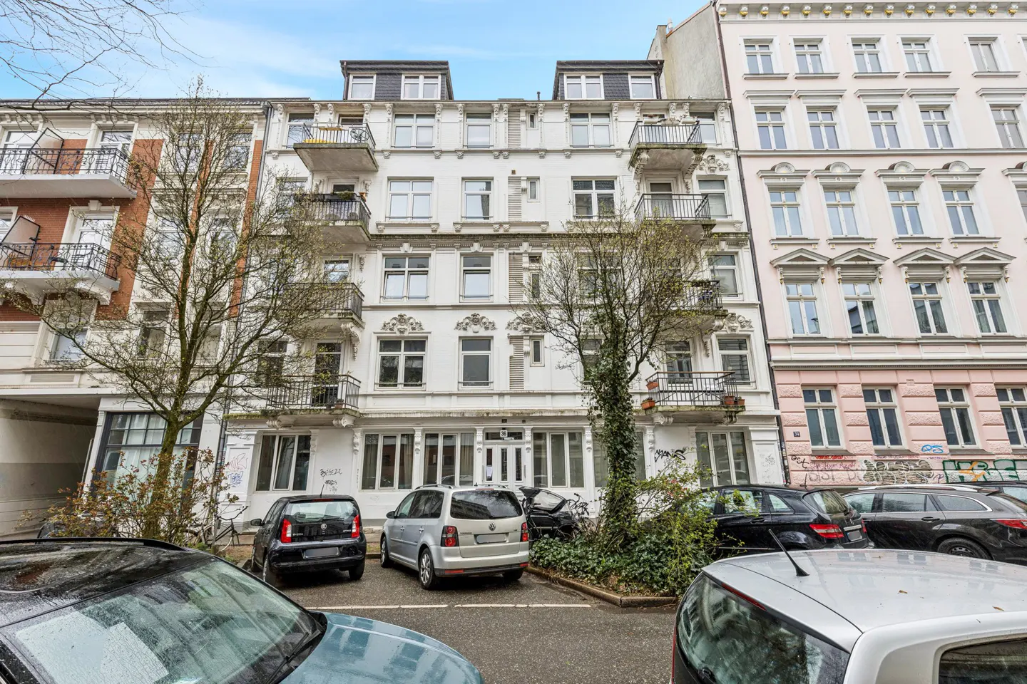 A white apartment building with black balconies and parked cars in front.