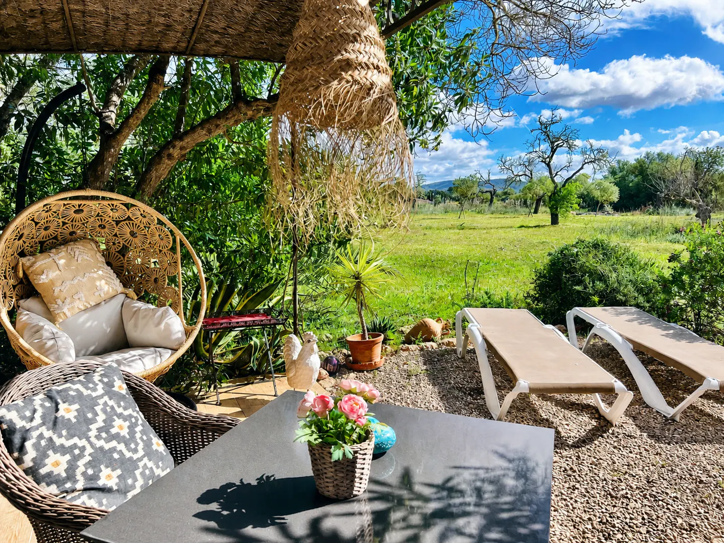 Outdoor patio with wicker furniture, lounge chairs, and a view of a green field under a blue sky with white clouds.