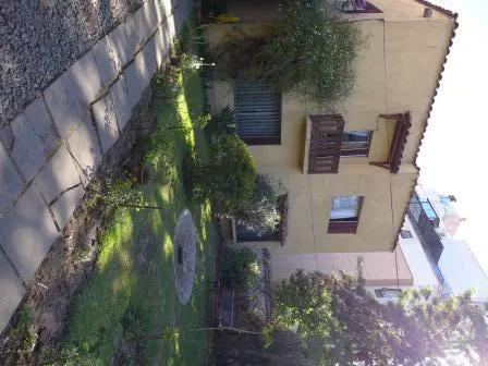 A tan building with a red tile roof is surrounded by a green lawn and trees. A stone path leads to the building.
