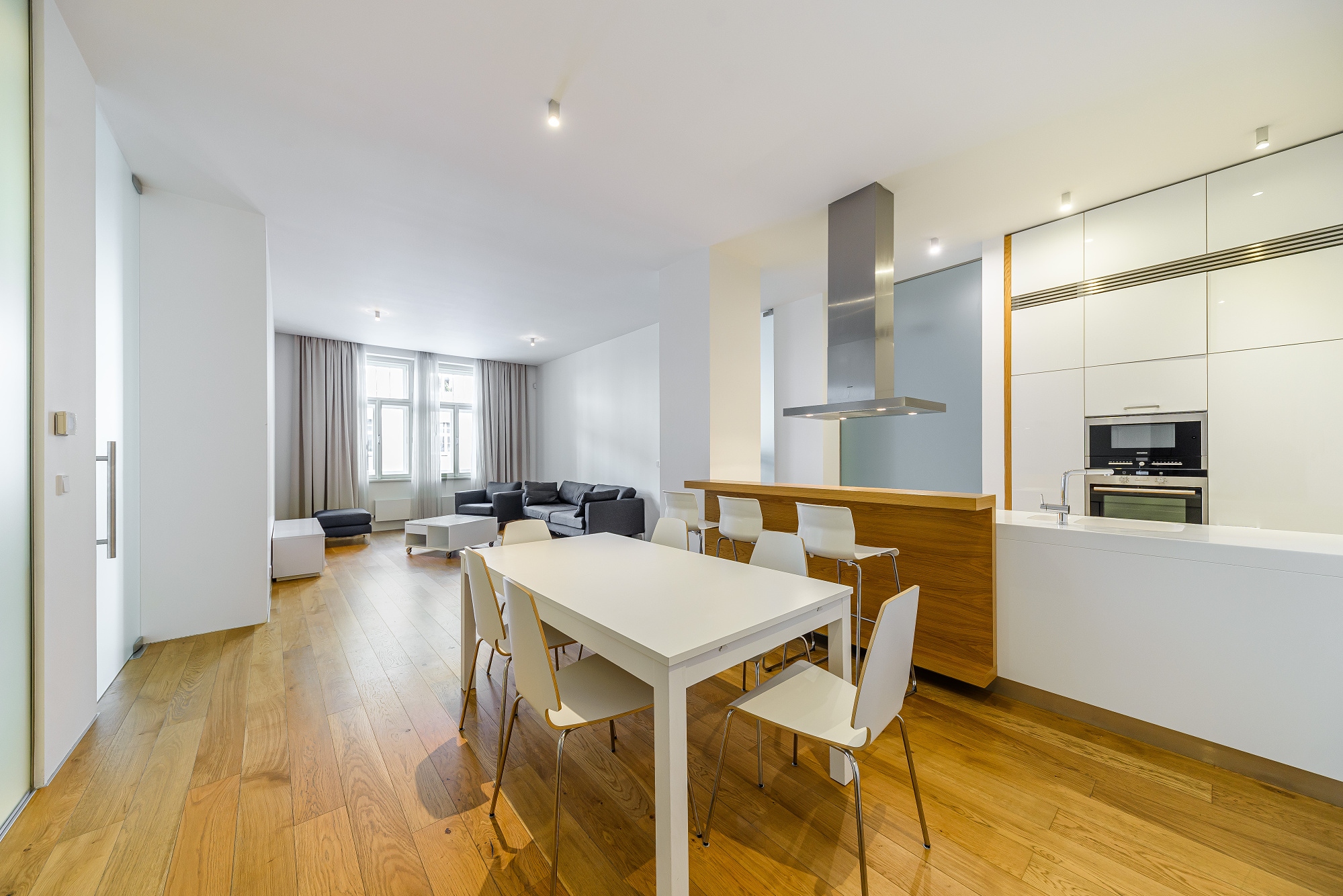 Modern open-plan apartment with a white dining set, wooden floors, and a sleek kitchen with white cabinets and a breakfast bar. [AI-generated text]