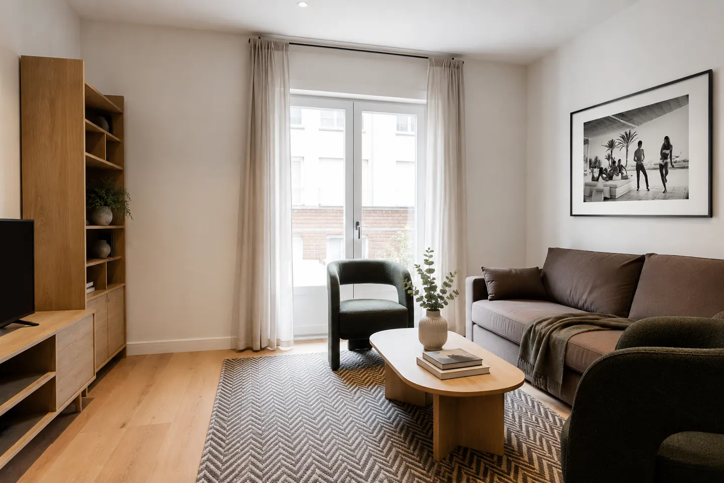Living room with wood floors, a brown sofa, and a dark green chair. A black and white photo hangs on the wall.