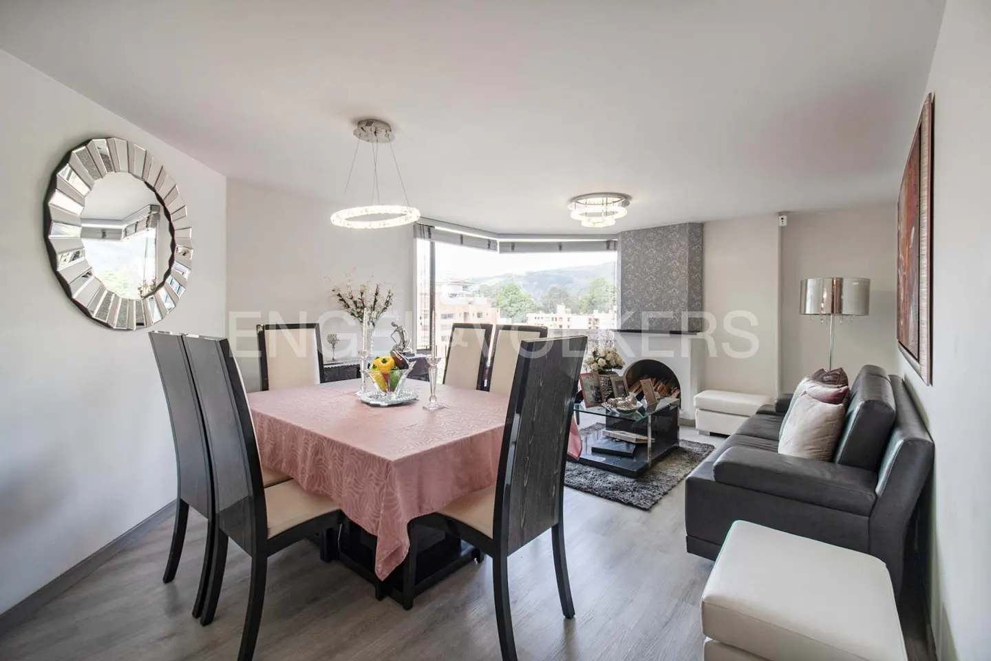 Open-concept living and dining area with gray sofa, dining table with pink tablecloth, and round mirror.