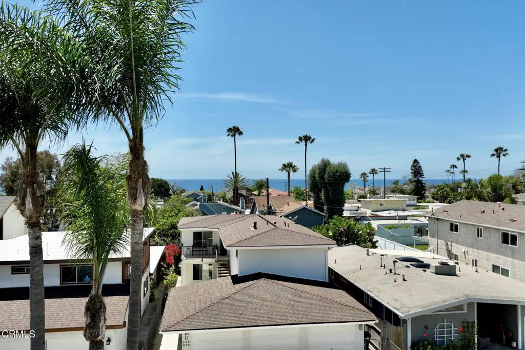 View of a neighborhood with houses and palm trees, with the ocean visible in the background under a clear blue sky.