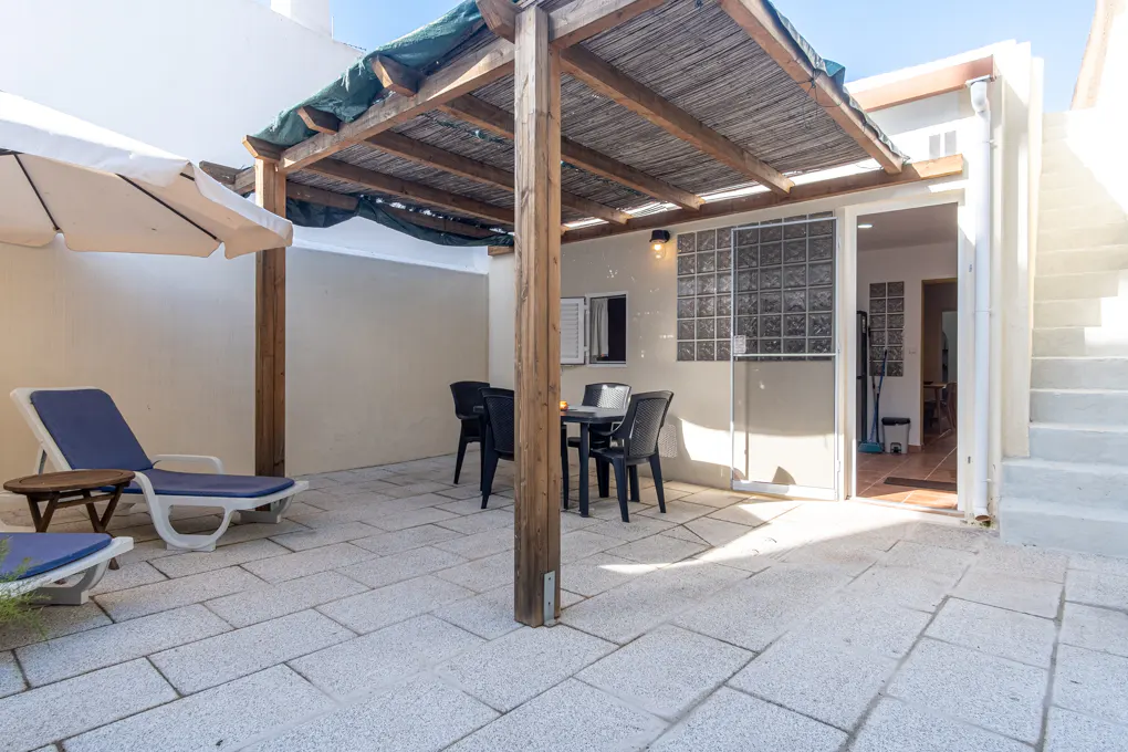 Outdoor patio with stone flooring, a wooden pergola, a blue lounge chair, and a black table with chairs.