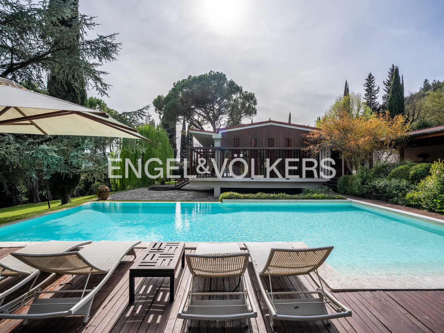 Outdoor pool with lounge chairs on a wooden deck. The Engel & Völkers logo is superimposed on the image.