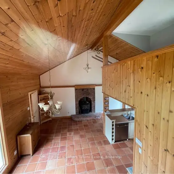 A high-angle view of a living room with wood-paneled walls and ceiling, a brick fireplace, and terracotta tile flooring.