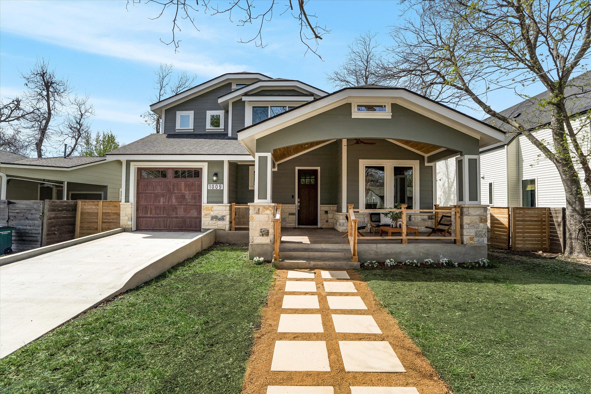 Two-story house with a brown garage door, a green porch, and a stone walkway.