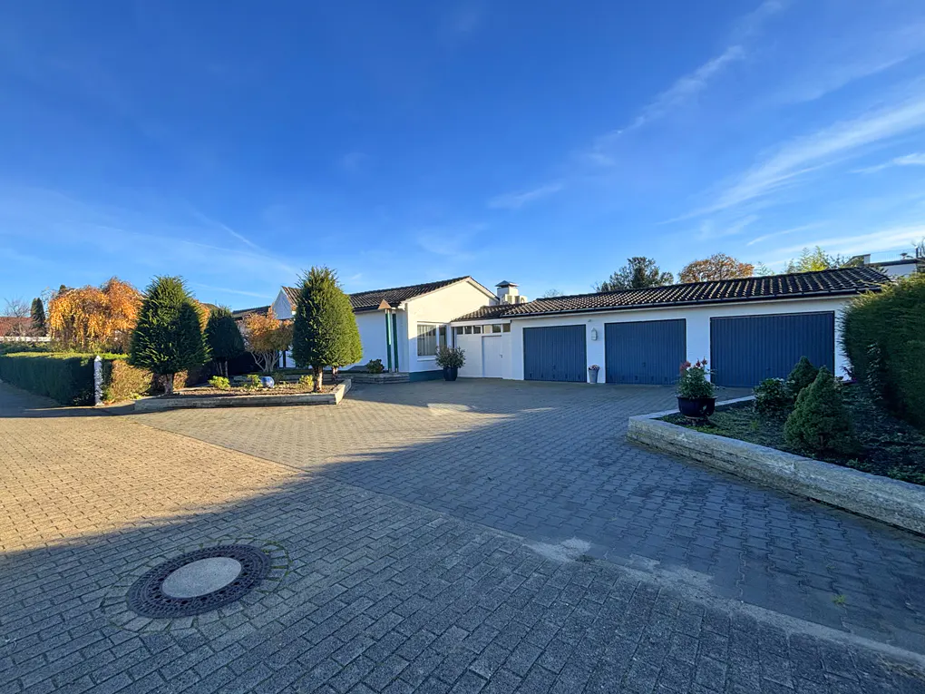 A white house with a blue garage door and a brick driveway under a clear blue sky.