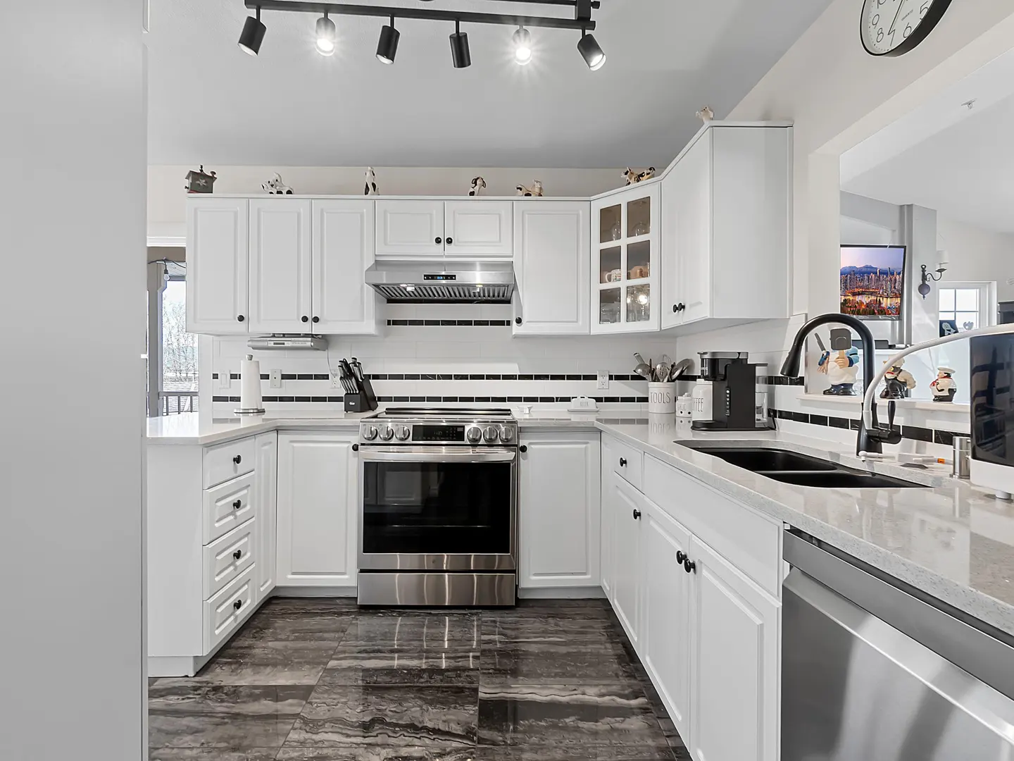 Modern white kitchen with stainless steel appliances, black and white tile backsplash, and dark marble-patterned tile floors.