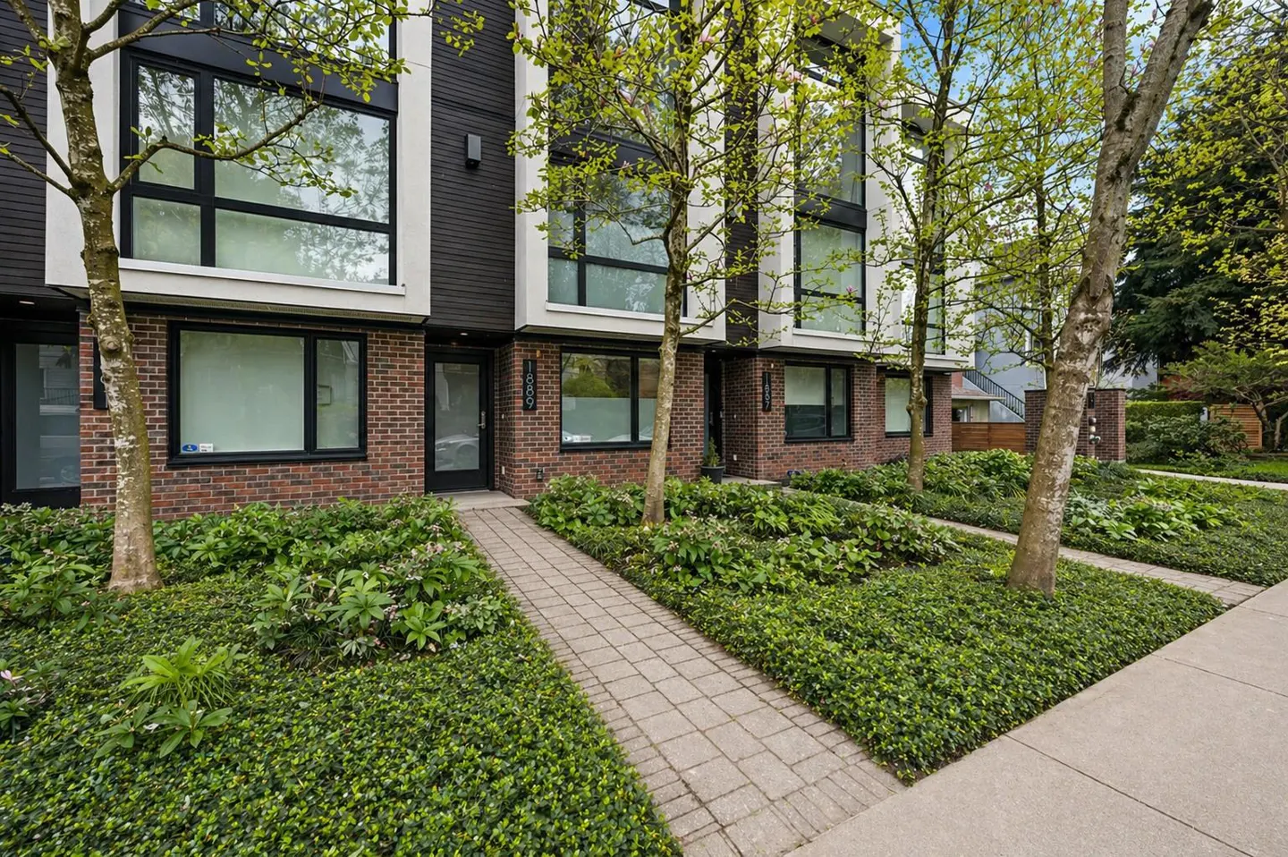 Row of modern townhouses with brick and dark siding, black framed windows, and green ground cover.