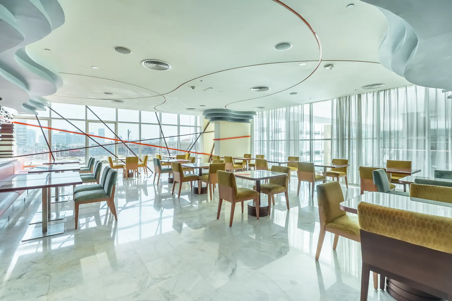 Bright, modern restaurant with marble floors, square tables, and upholstered chairs. Large windows offer city views.