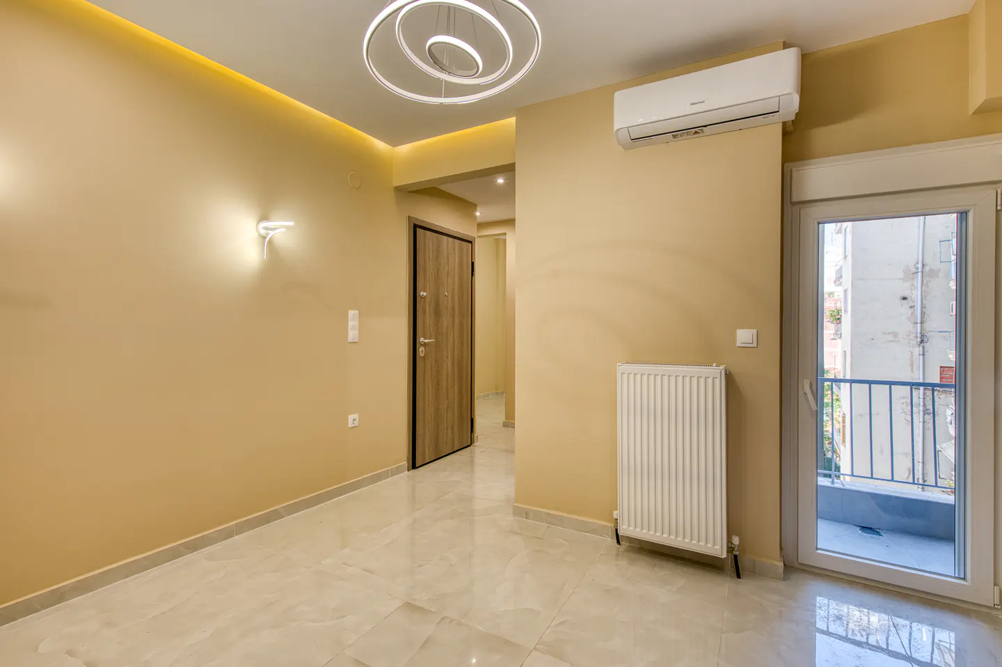A bright, empty room with beige walls, a modern light fixture, and a door leading to a balcony.