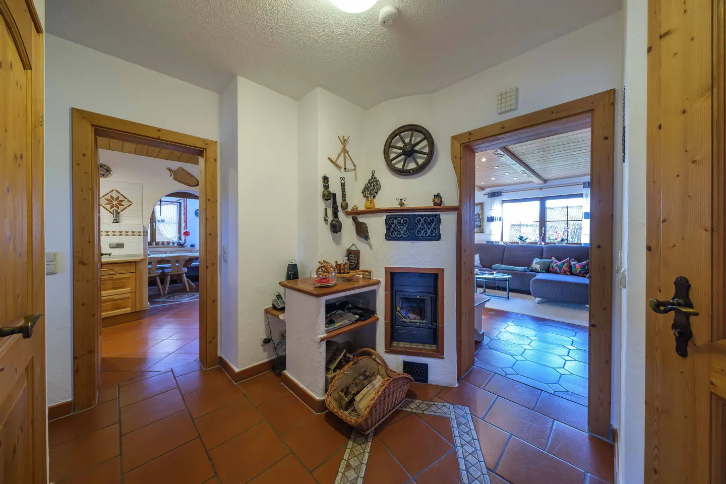 Hallway with terracotta tile floor, wood-burning stove, and doorways to kitchen and living room.