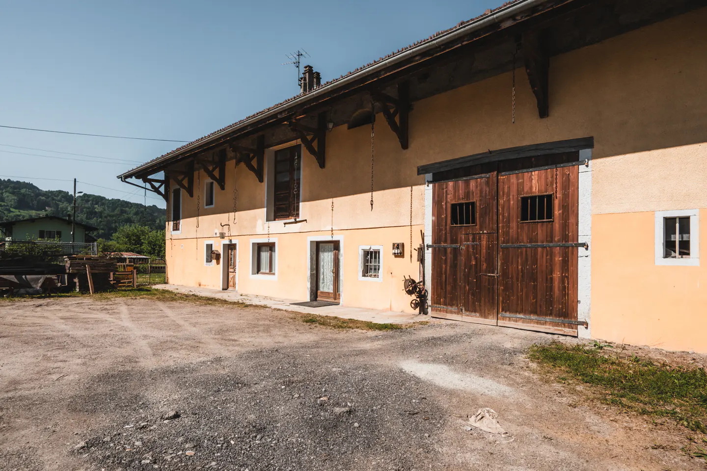 Exterior view of a two-story yellow farmhouse with large wooden barn doors and a gravel driveway.