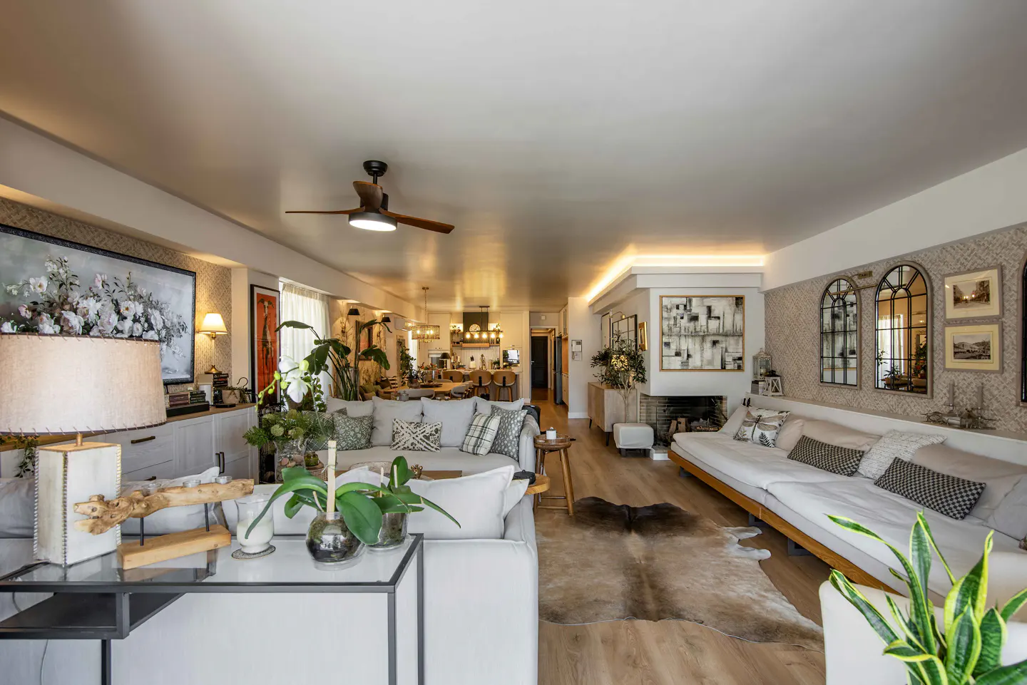 Spacious open-plan living room with white sofas, a cowhide rug, modern lighting, and a view into the kitchen.