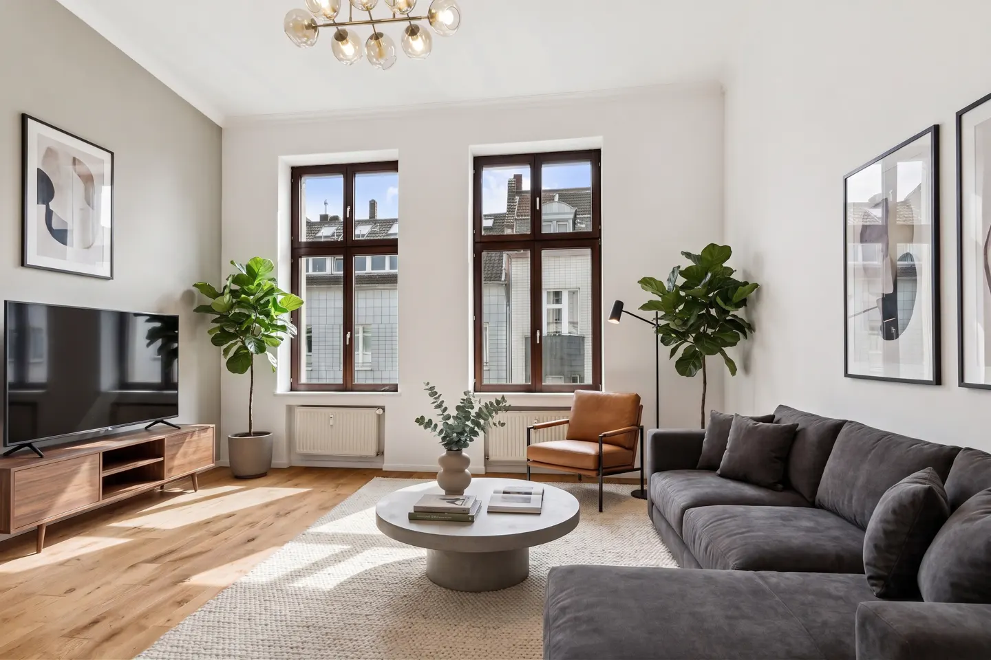 Modern living room with a grey sectional sofa, round coffee table, leather armchair, TV, and two large potted plants.
