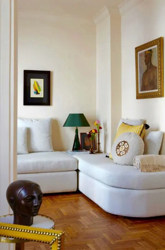 Interior of a living room with white walls, a white sectional sofa, and hardwood floors. Artwork and a green lamp decorate the space.