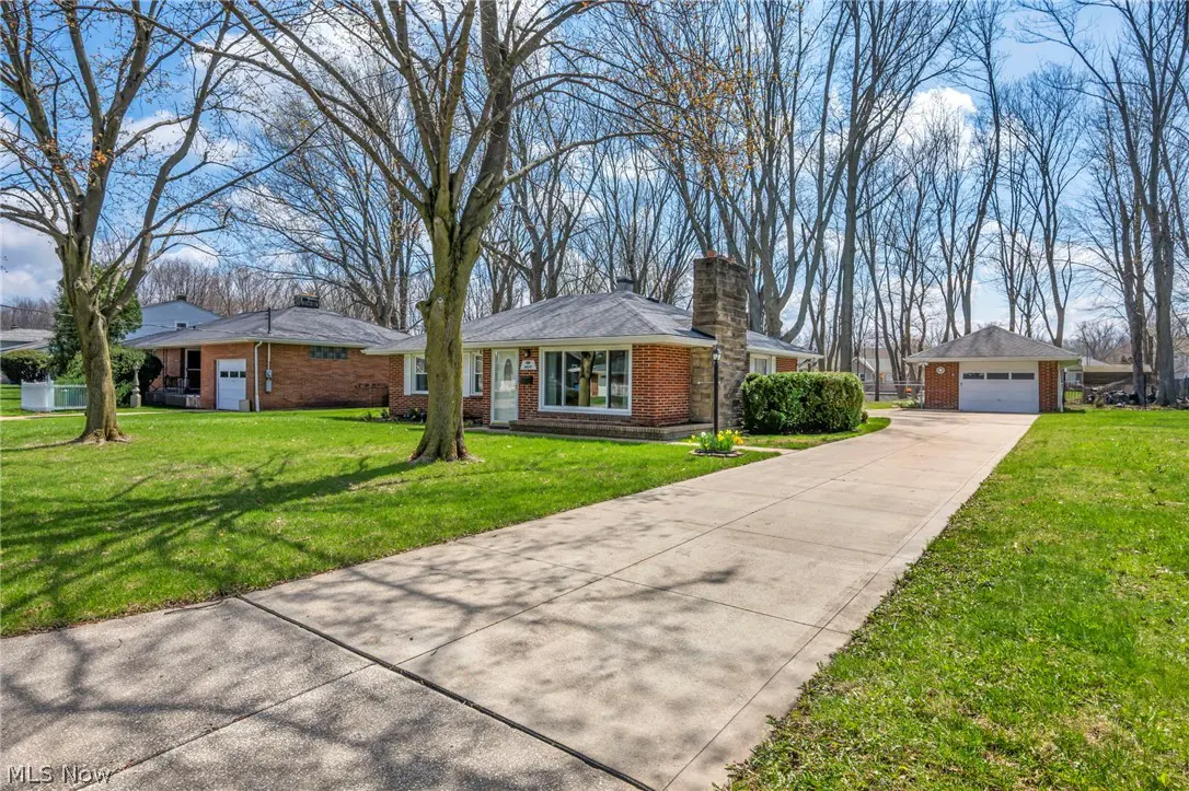 A red brick ranch-style house with a long driveway and detached garage on a sunny day.