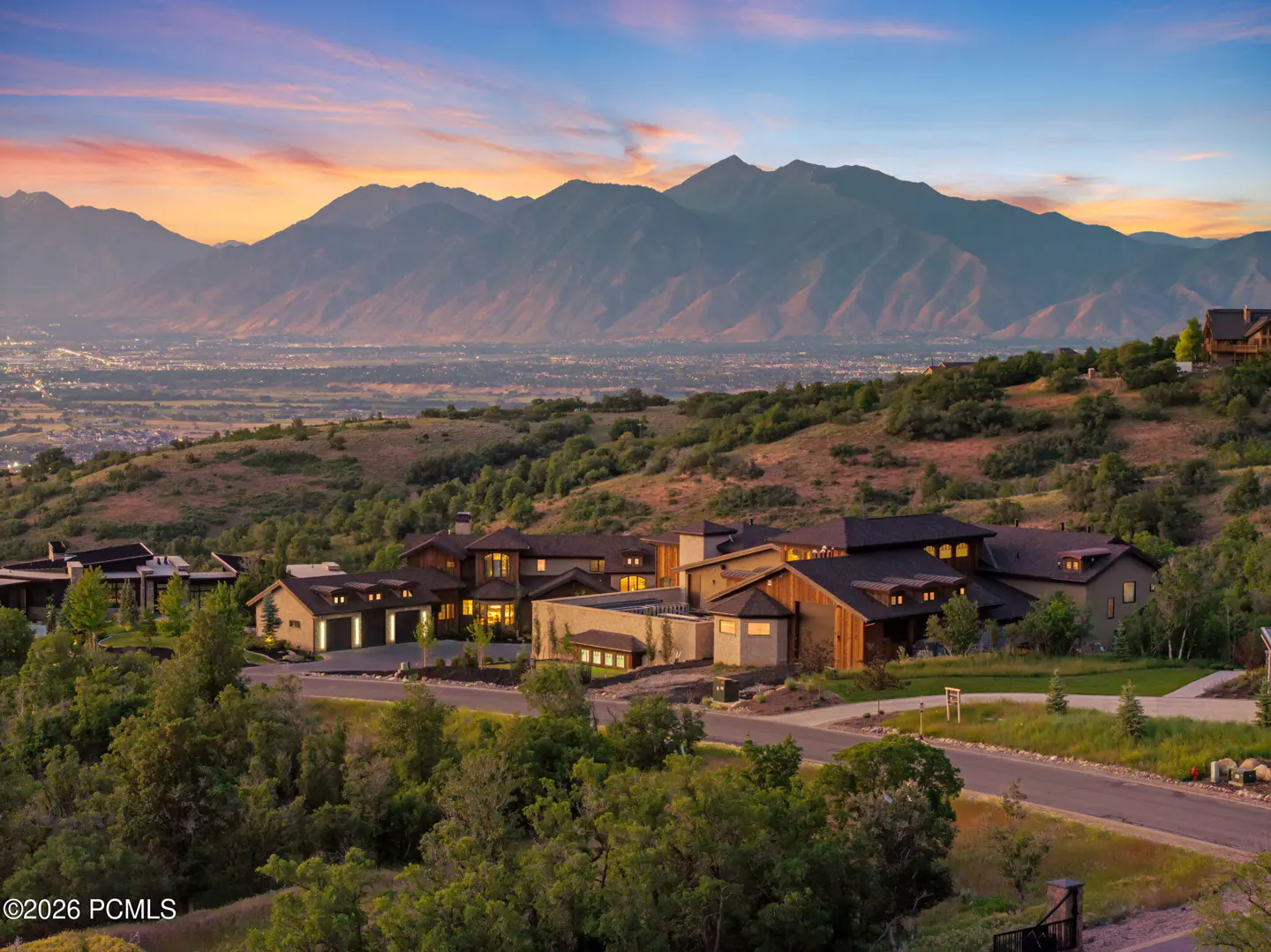 Luxury homes on a hillside with mountain views at sunset. Houses are tan and brown with dark roofs.