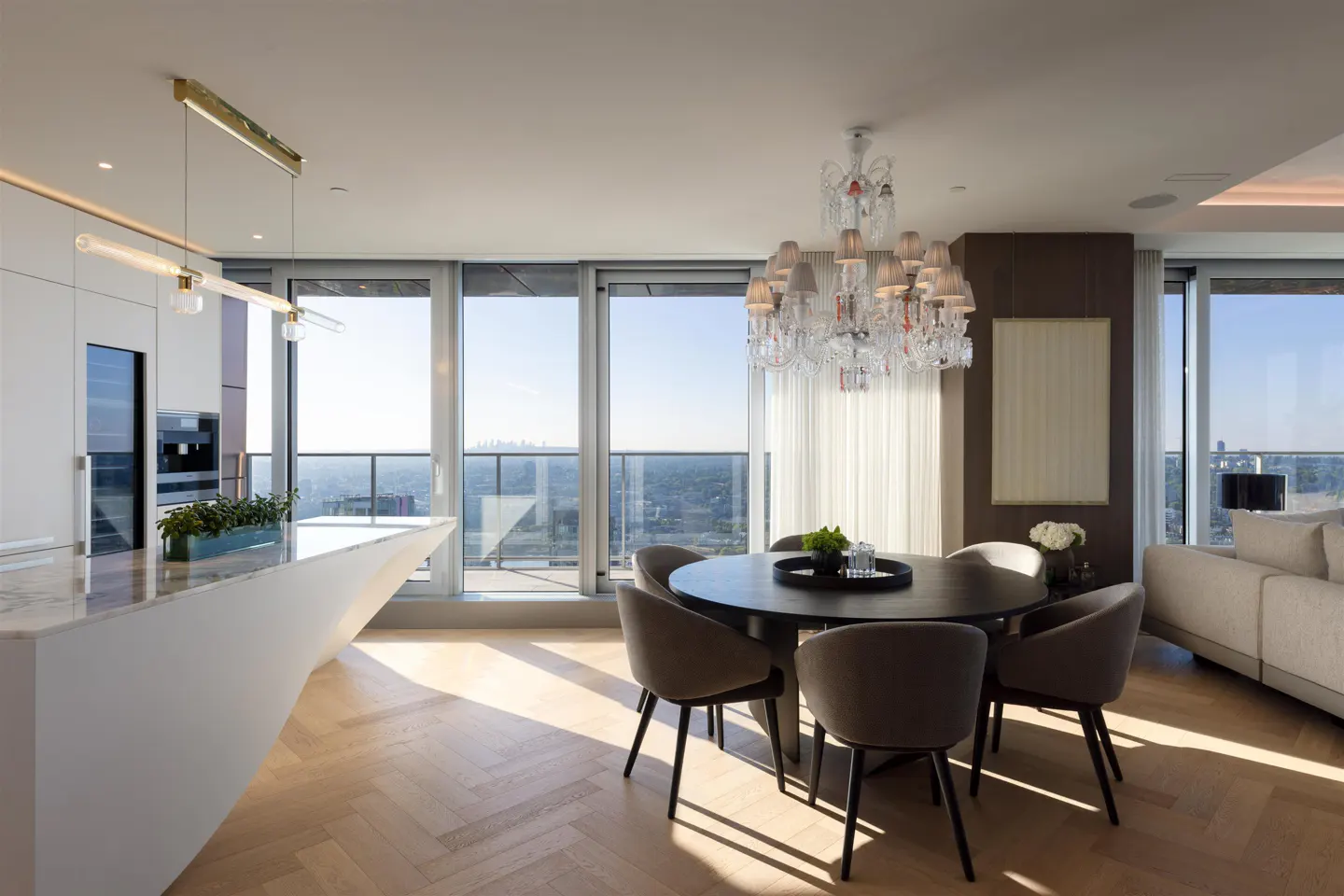 Bright, modern condo interior with a round dining table, crystal chandelier, and floor-to-ceiling windows with a city view.