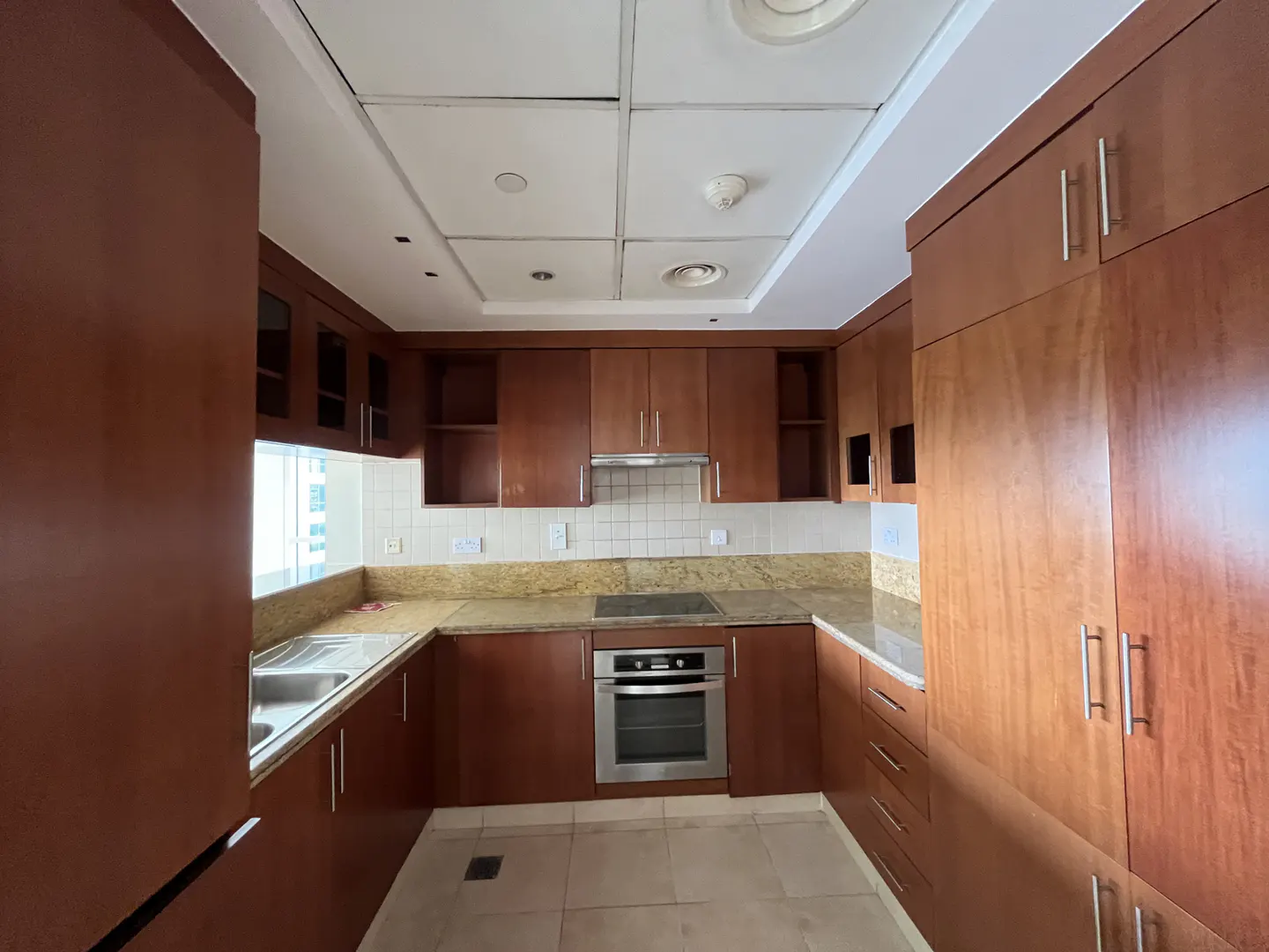 A kitchen with brown cabinets, stainless steel appliances, and light beige tile flooring.