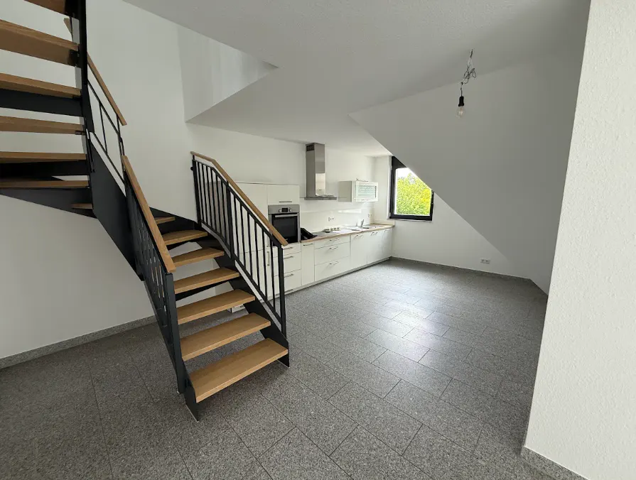A modern apartment interior with a staircase, white kitchen, and gray tiled floor.