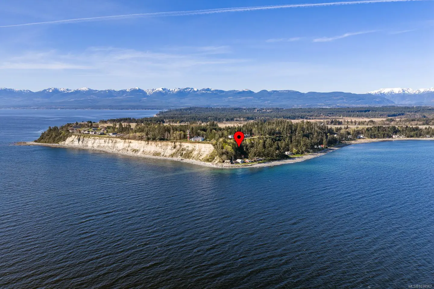 Aerial view of a coastal cliff with a red location pin marking a property surrounded by trees, overlooking the ocean.