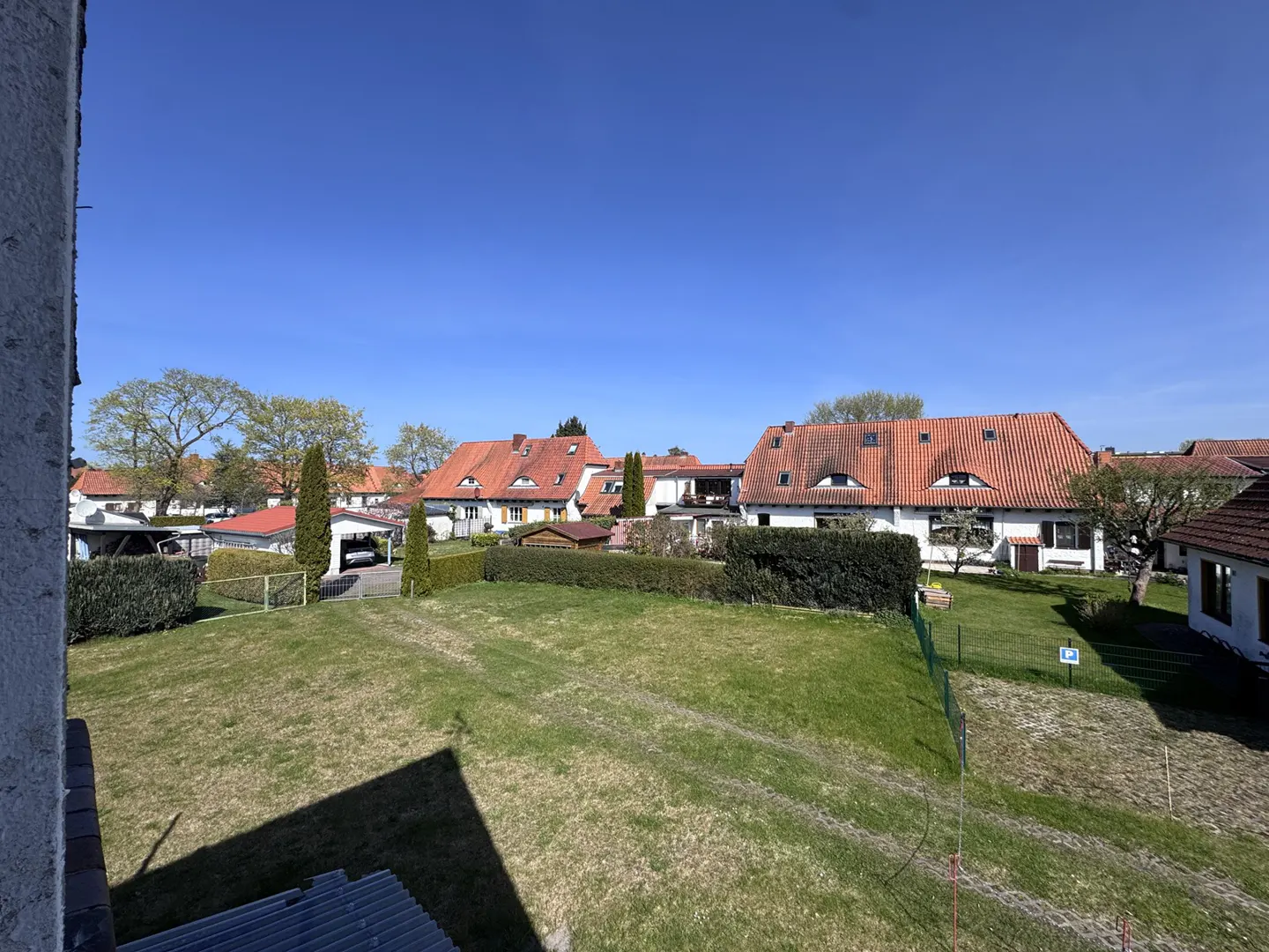 View of a green lawn and houses with red roofs under a clear blue sky.