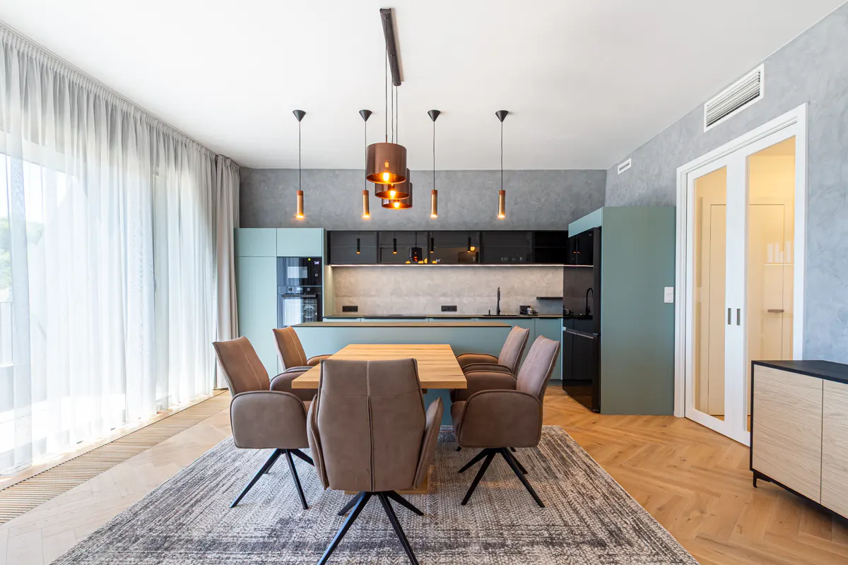 Modern dining area with a wooden table, brown swivel chairs, and a sleek kitchen with sage green cabinets and pendant lights.