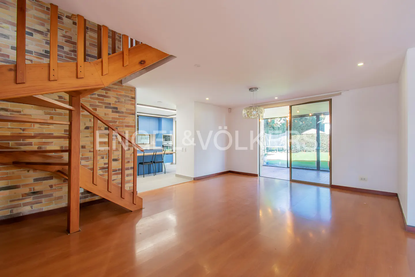 Open-concept living room with wood floors, brick wall, spiral staircase, and sliding glass doors to a green lawn.