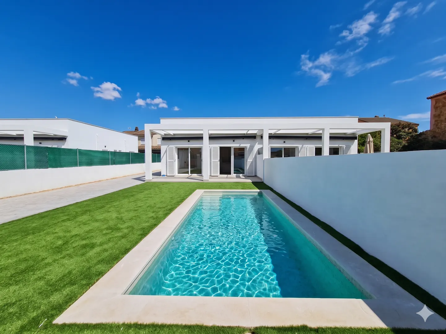 A modern white house with a rectangular pool and green lawn under a blue sky.