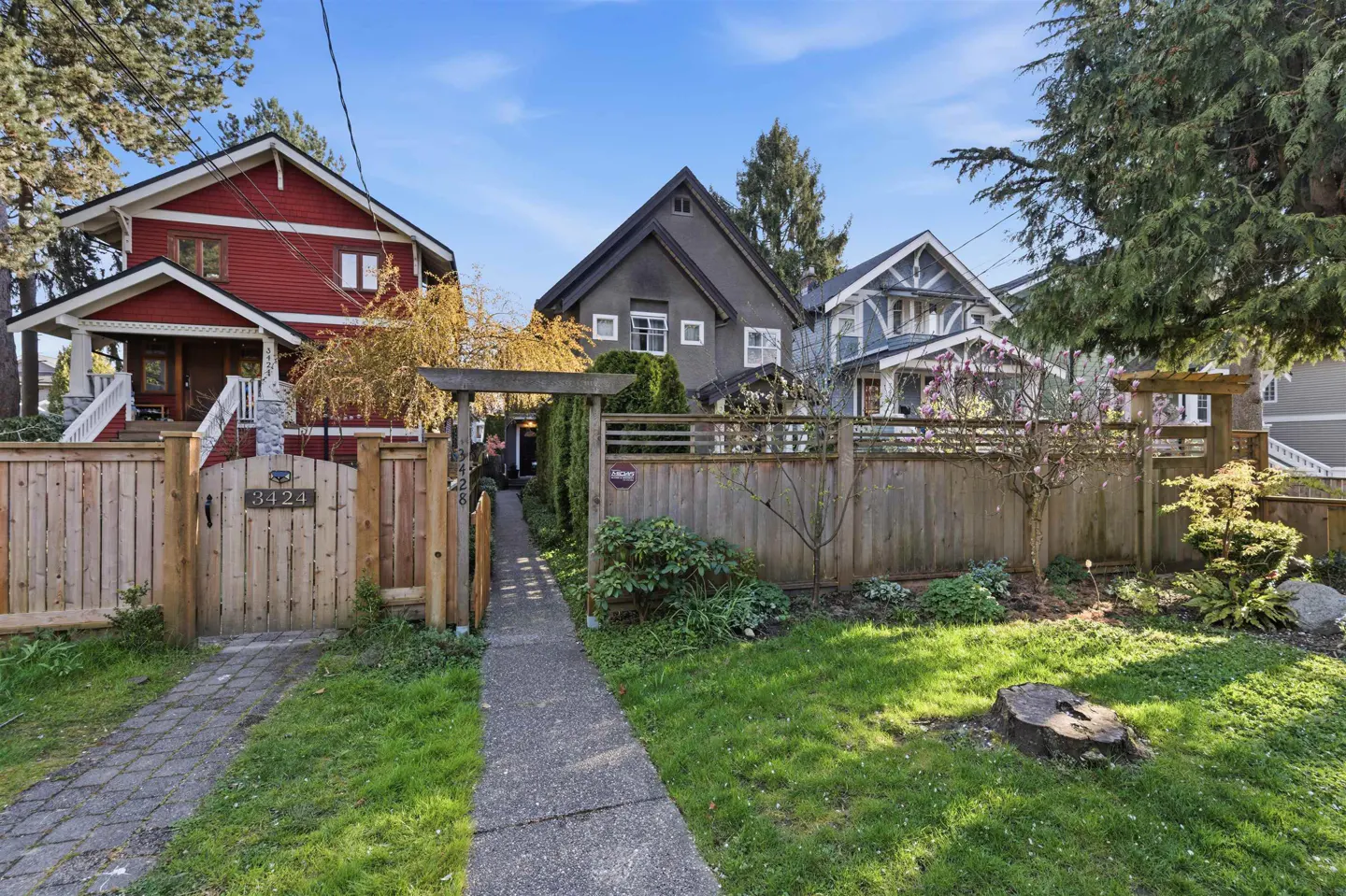 Street view of three houses with wooden fences and green lawns under a blue sky.