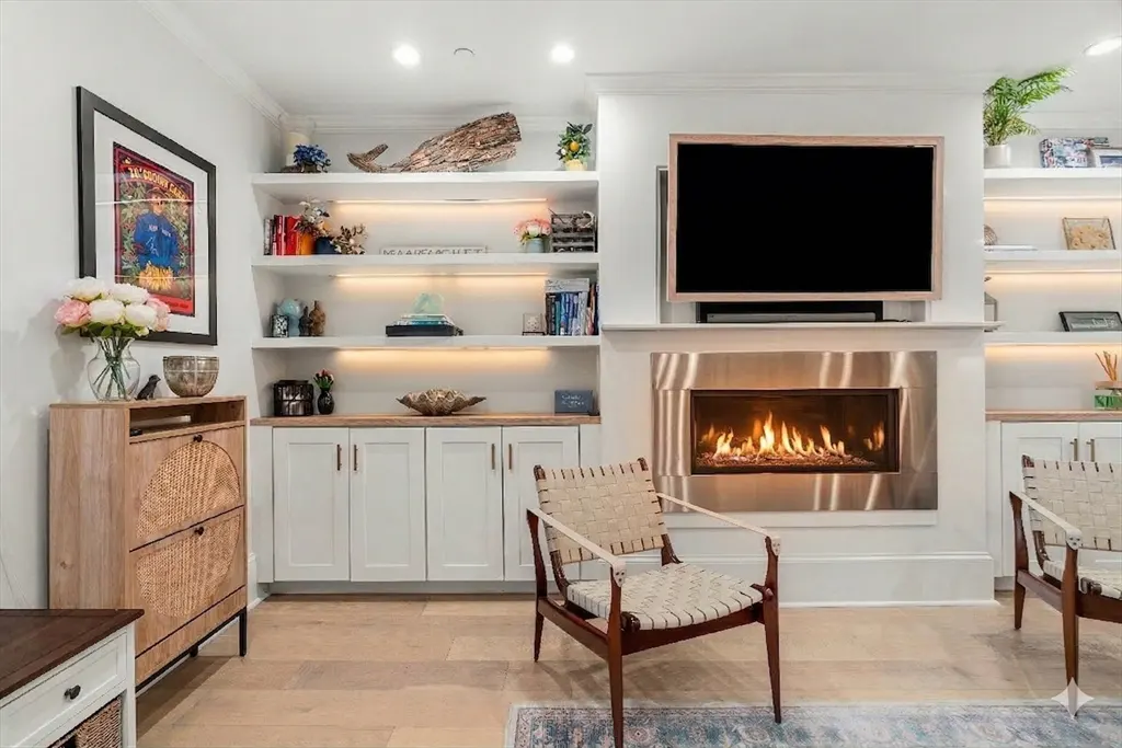 Living room with a fireplace, TV, built-in shelves, and two woven chairs. The shelves are decorated with books and decorative items.