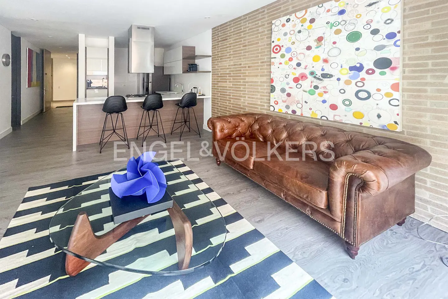 A modern living room with a brown leather sofa, a glass coffee table, and a black and white rug.