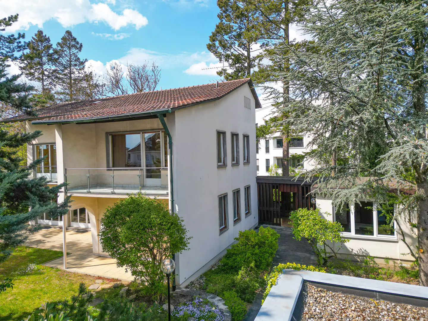 Exterior view of a two-story white house with a red tile roof, surrounded by green trees and a blue sky.