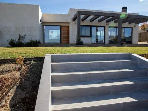 Modern home exterior with gray steps leading to a lawn and a white house with large windows and a dark pergola.