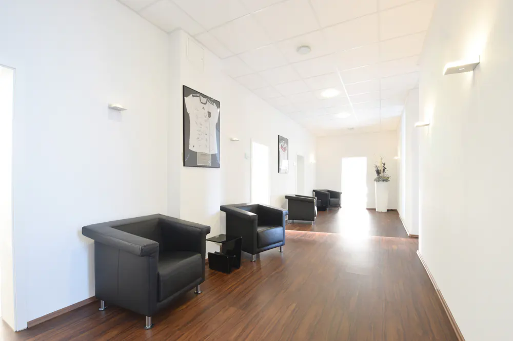Hallway with dark wood floors, white walls, and black leather chairs. Framed art hangs on the walls.