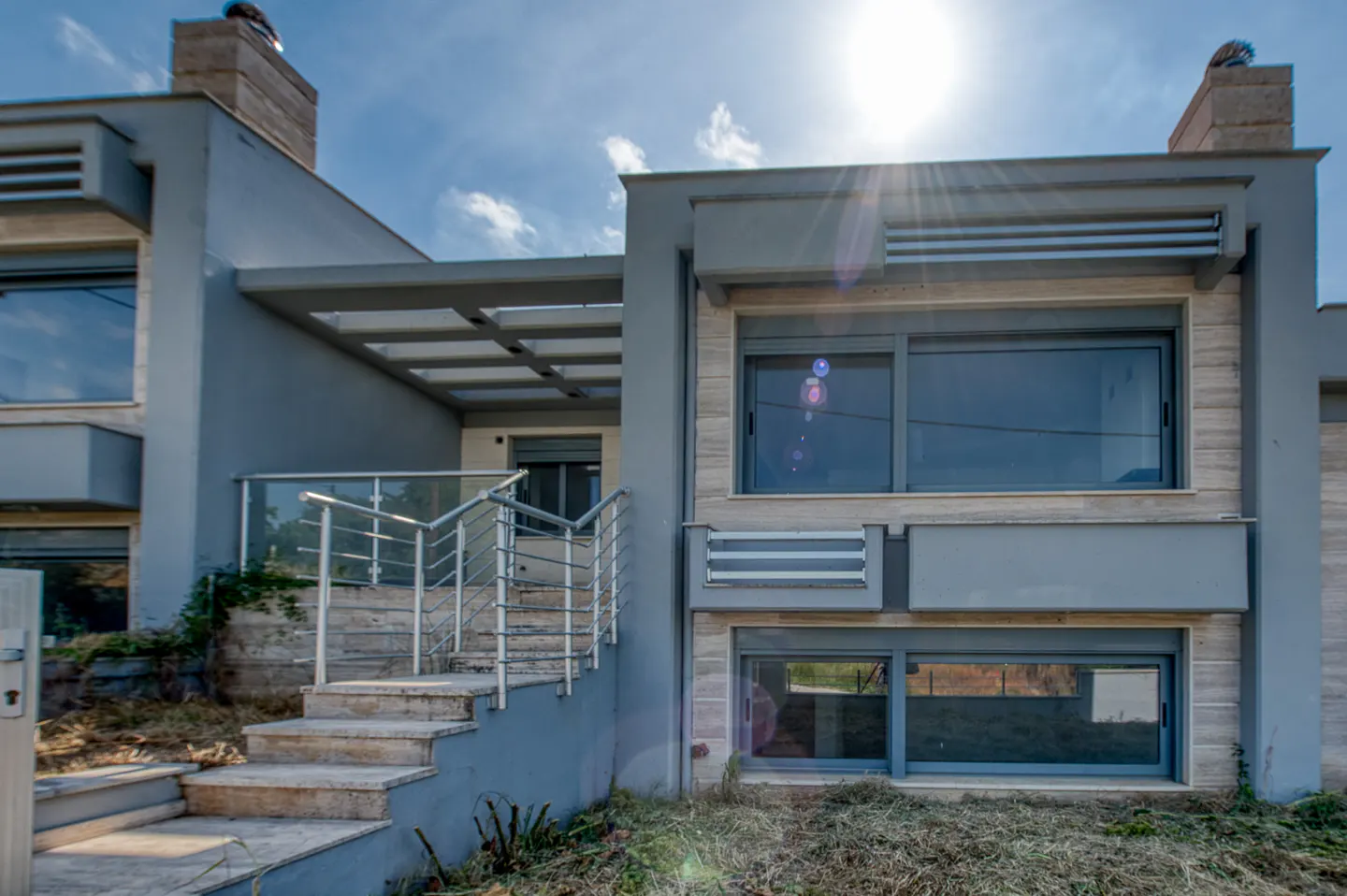 Modern two-story home with gray exterior, stone accents, large windows, and a staircase with a metal railing.