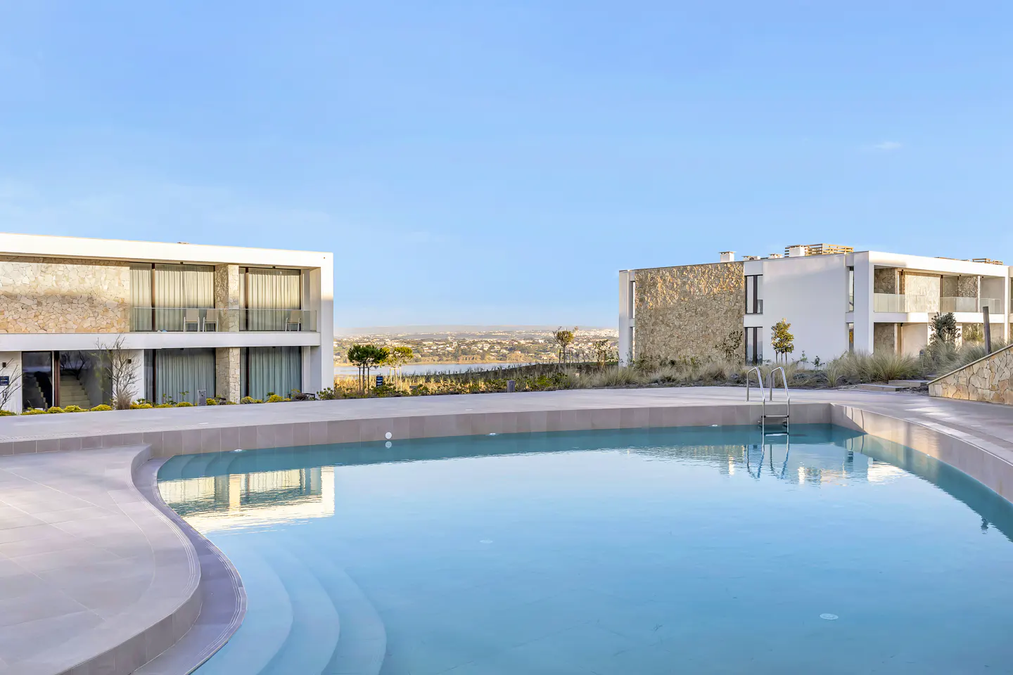 Luxury villas with a pool. Modern white buildings with stone accents overlook a blue pool and distant cityscape under a clear sky.