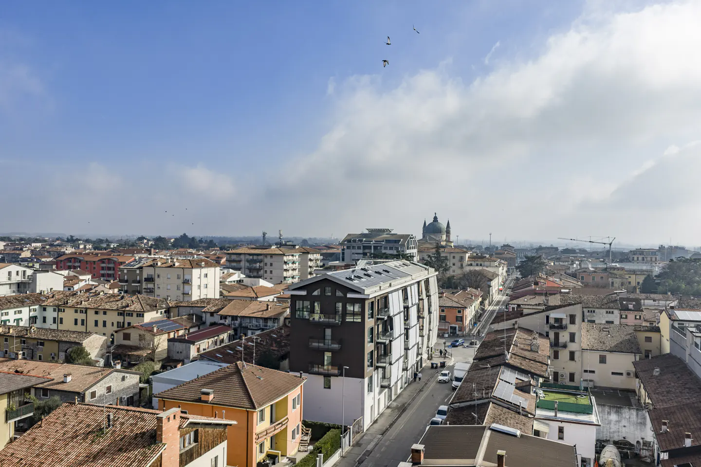 Cityscape view with buildings, terracotta roofs, and a church dome under a blue sky with scattered clouds.